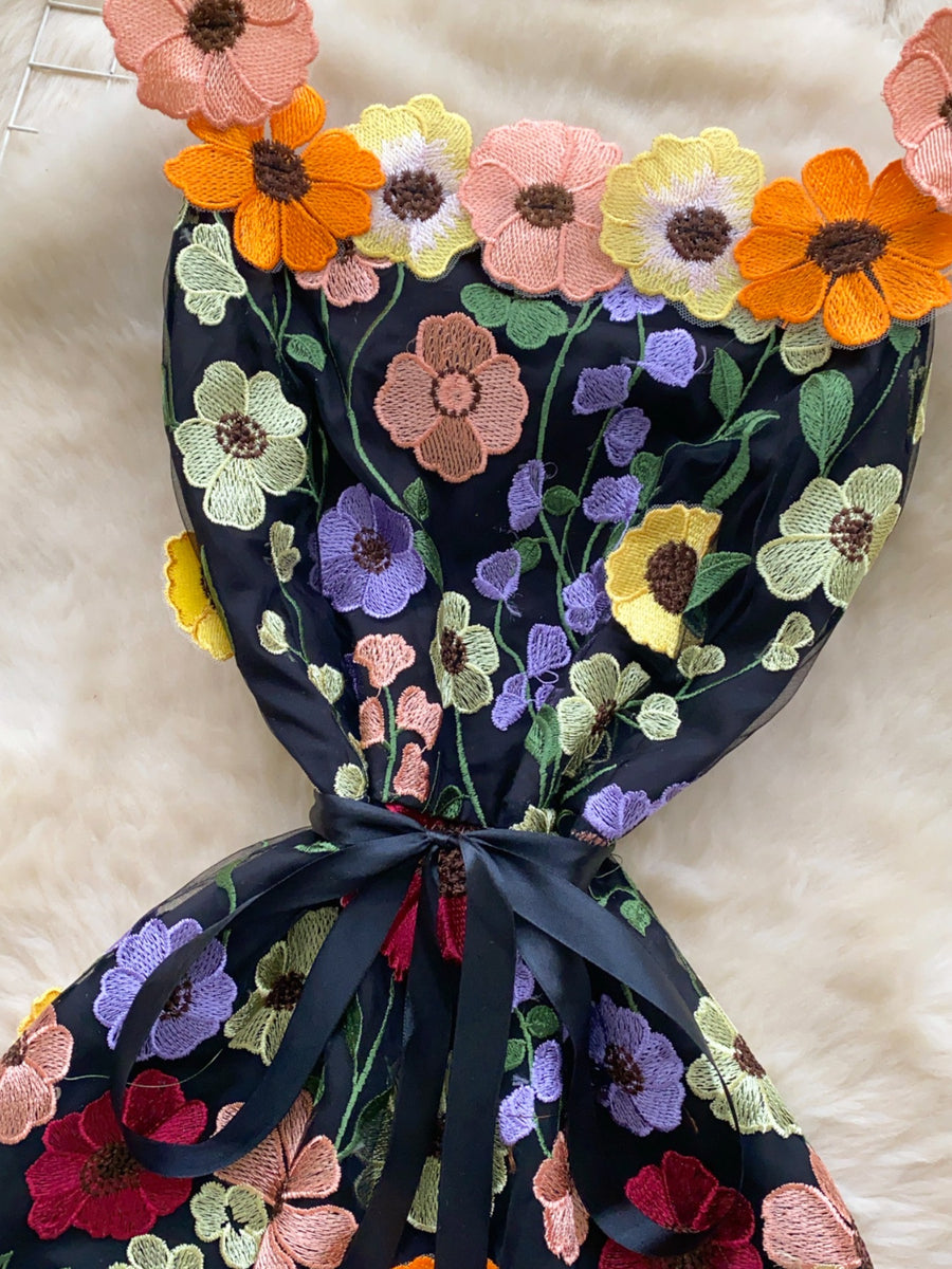Black mini dress with colorful floral embroidery and a bow detail.