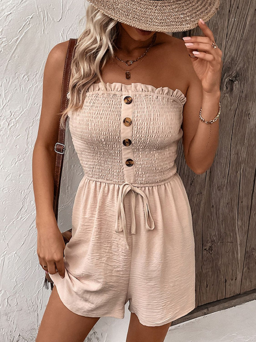 Tan smocked bodice romper with button front and tie waist, styled with a straw hat.