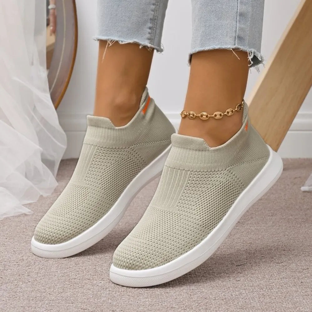Lightweight knit slip-on sneakers in off-white with white soles and orange accents.