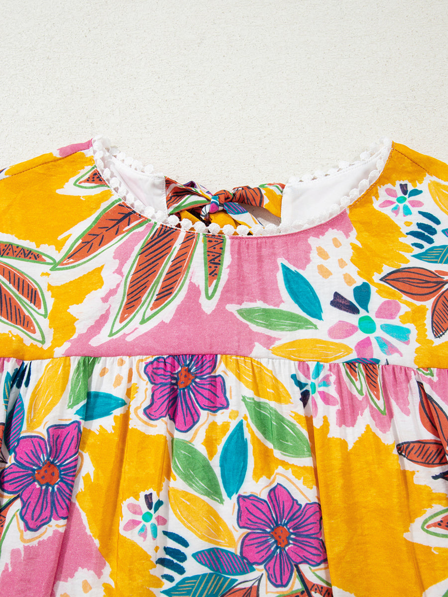 Print bell sleeve mini dress with colorful floral pattern, white pom-pom trim, and back tie detail.
