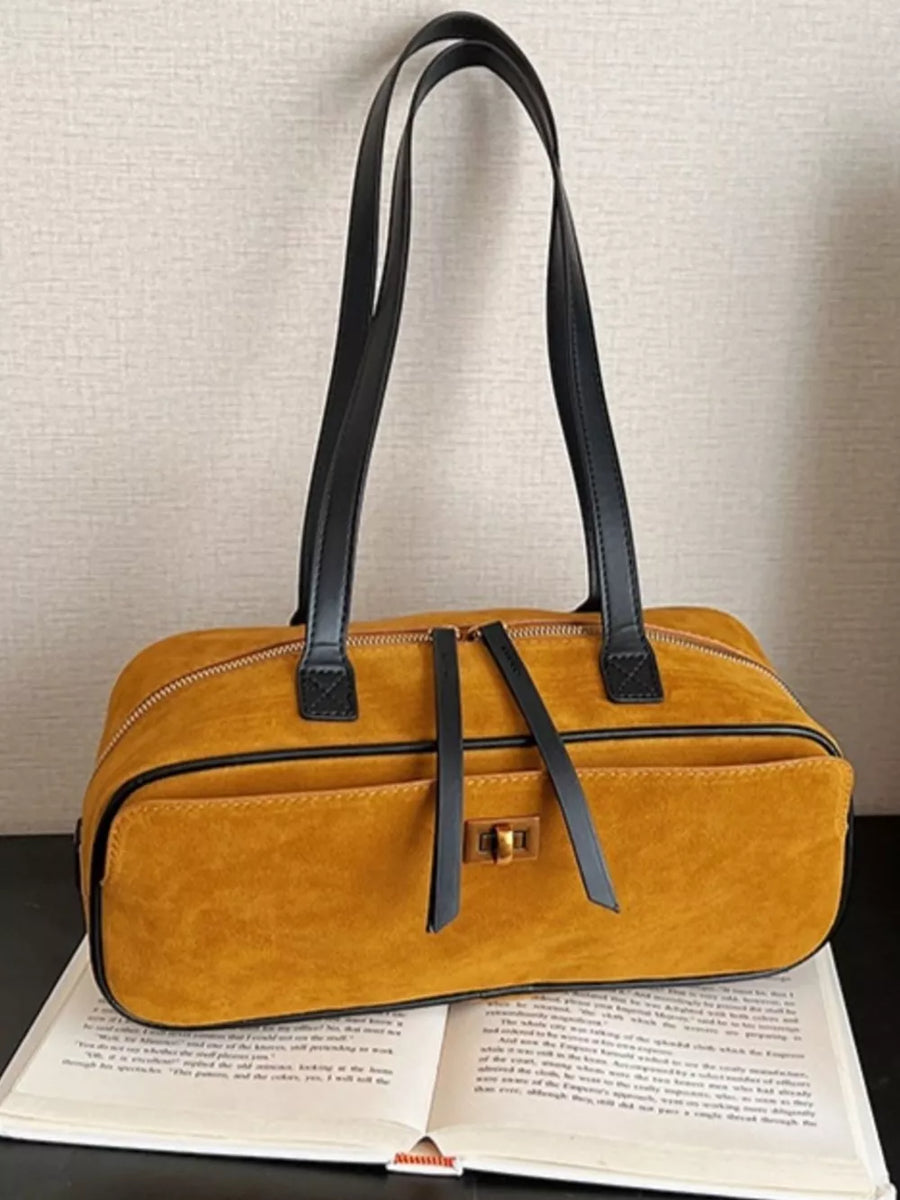 Yellow suede shoulder bag with gold clasp and black straps on an open book.