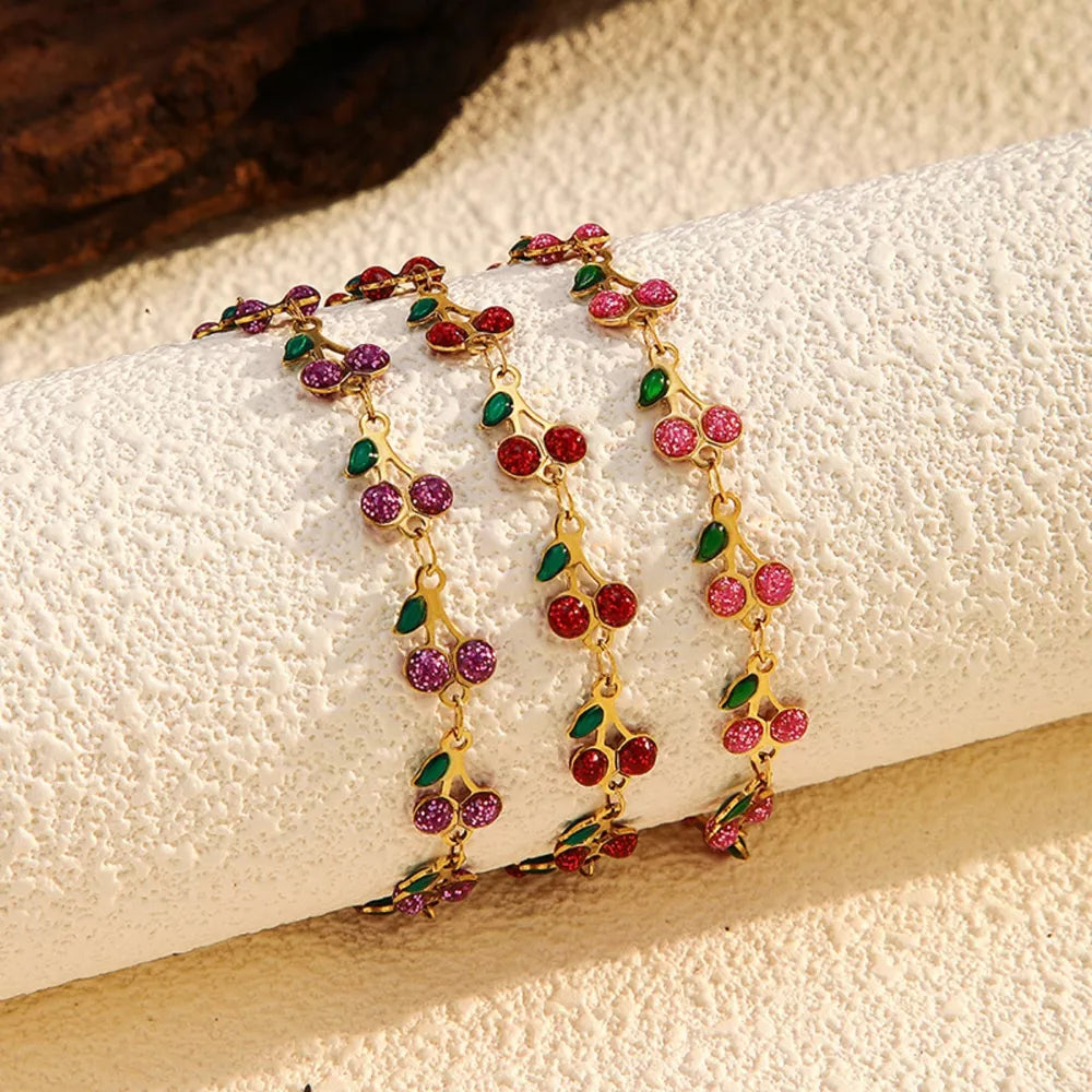 Gold-plated cherry cluster bracelet with red, pink, and purple gems and green leaves.