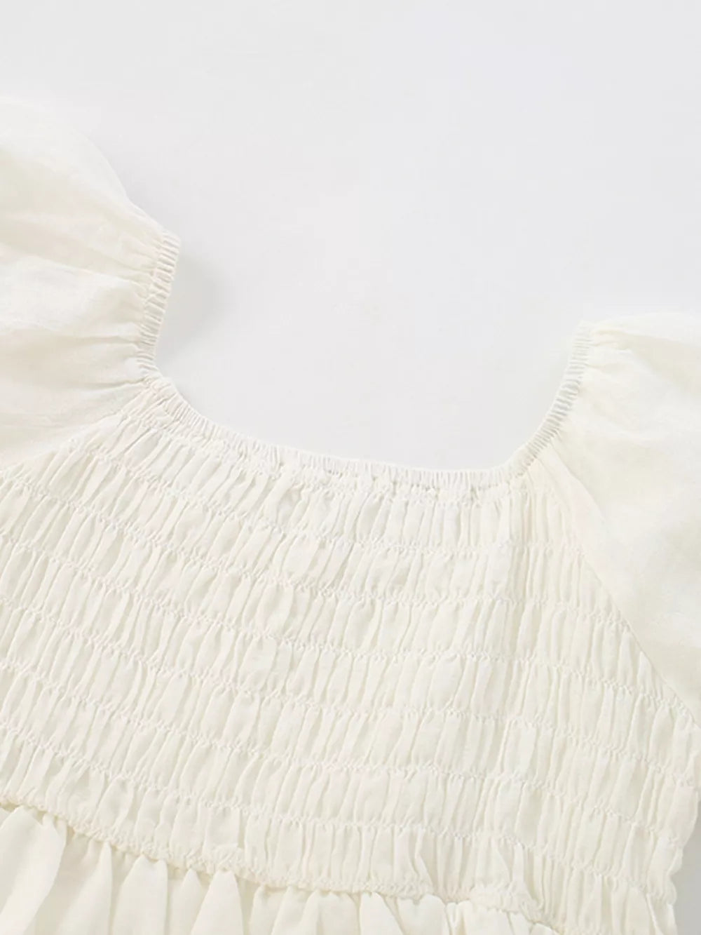 Cream smocked toddler dress with puff sleeves and tiered skirt detail.