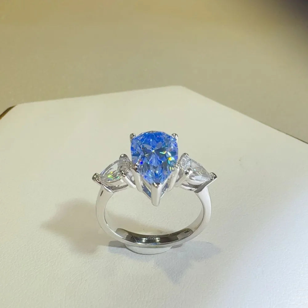 Silver trilogy ring with a large pear cut blue moissanite and two smaller pear cut side stones.