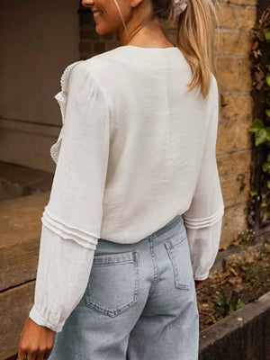 White lace ruffle V-neck blouse with long sleeves and tiered cuff detail.