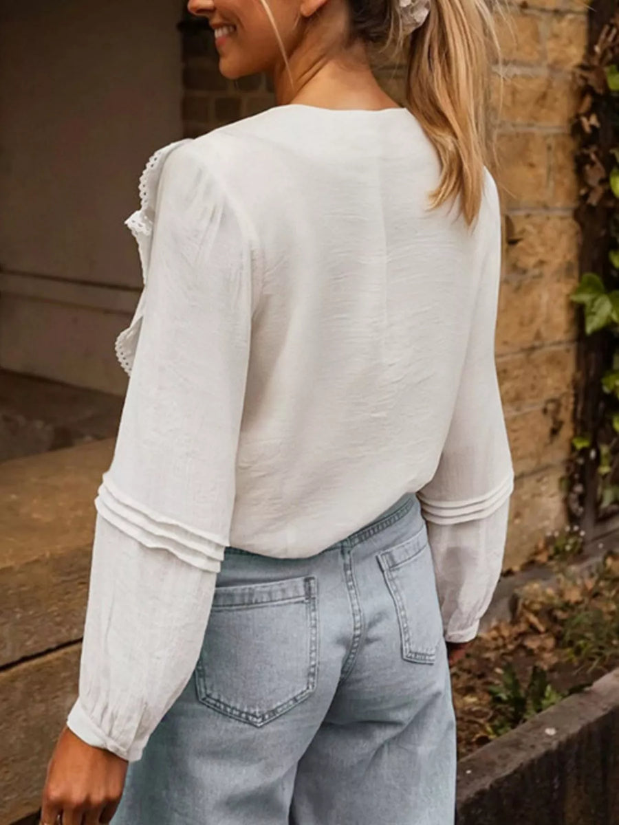 White lace ruffle V-neck blouse with long sleeves and tiered cuff detail.