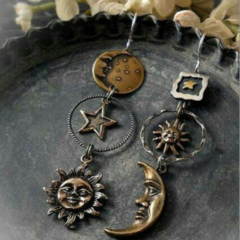 Cosmic asymmetry drop earrings in copper feature sun, moon, and star charms with mixed metal details.