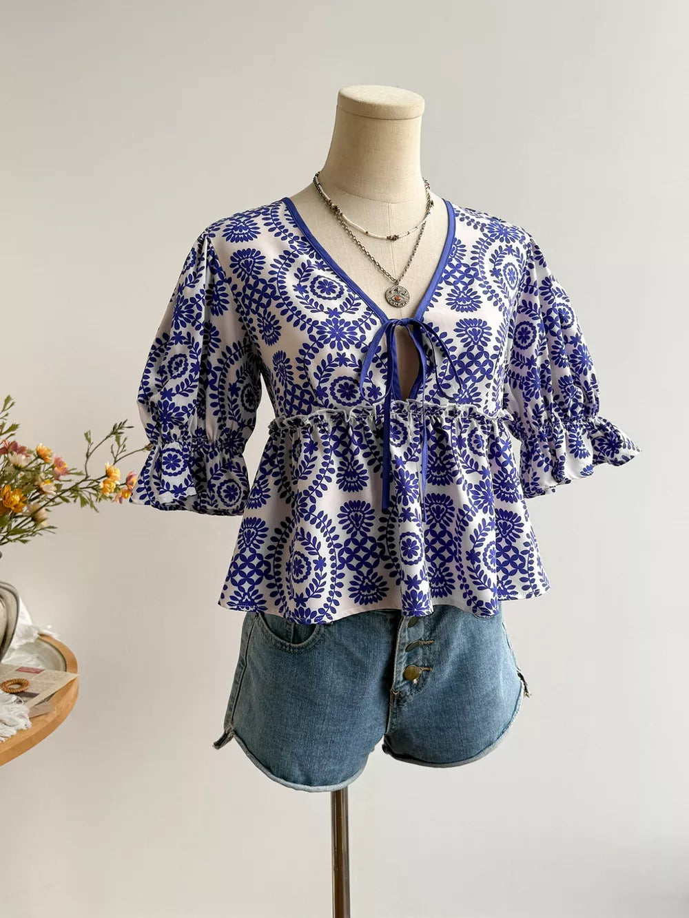 Chic floral tie-front blouse with 3/4 sleeves and ruffled cuffs, paired with denim shorts.