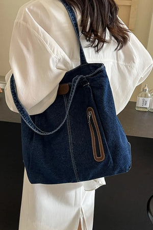 Denim tote bag with leather trim and front zipper pocket.
