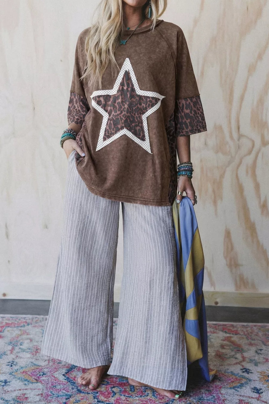 Brown graphic tee with leopard print star and cheetah print sleeves, paired with grey striped wide-leg pants.