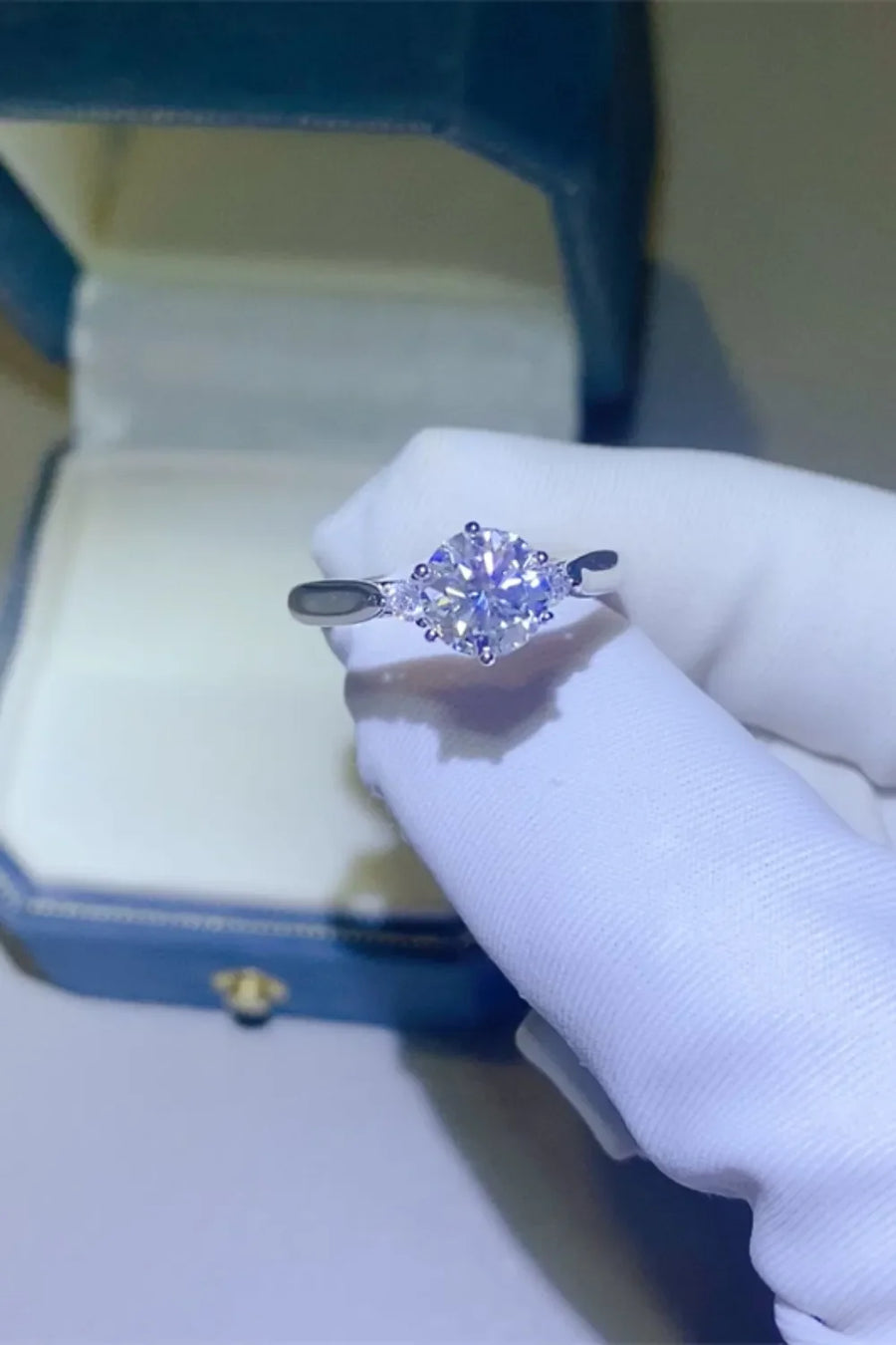 Silver moissanite trilogy engagement ring with a central round-cut stone and two smaller stones.