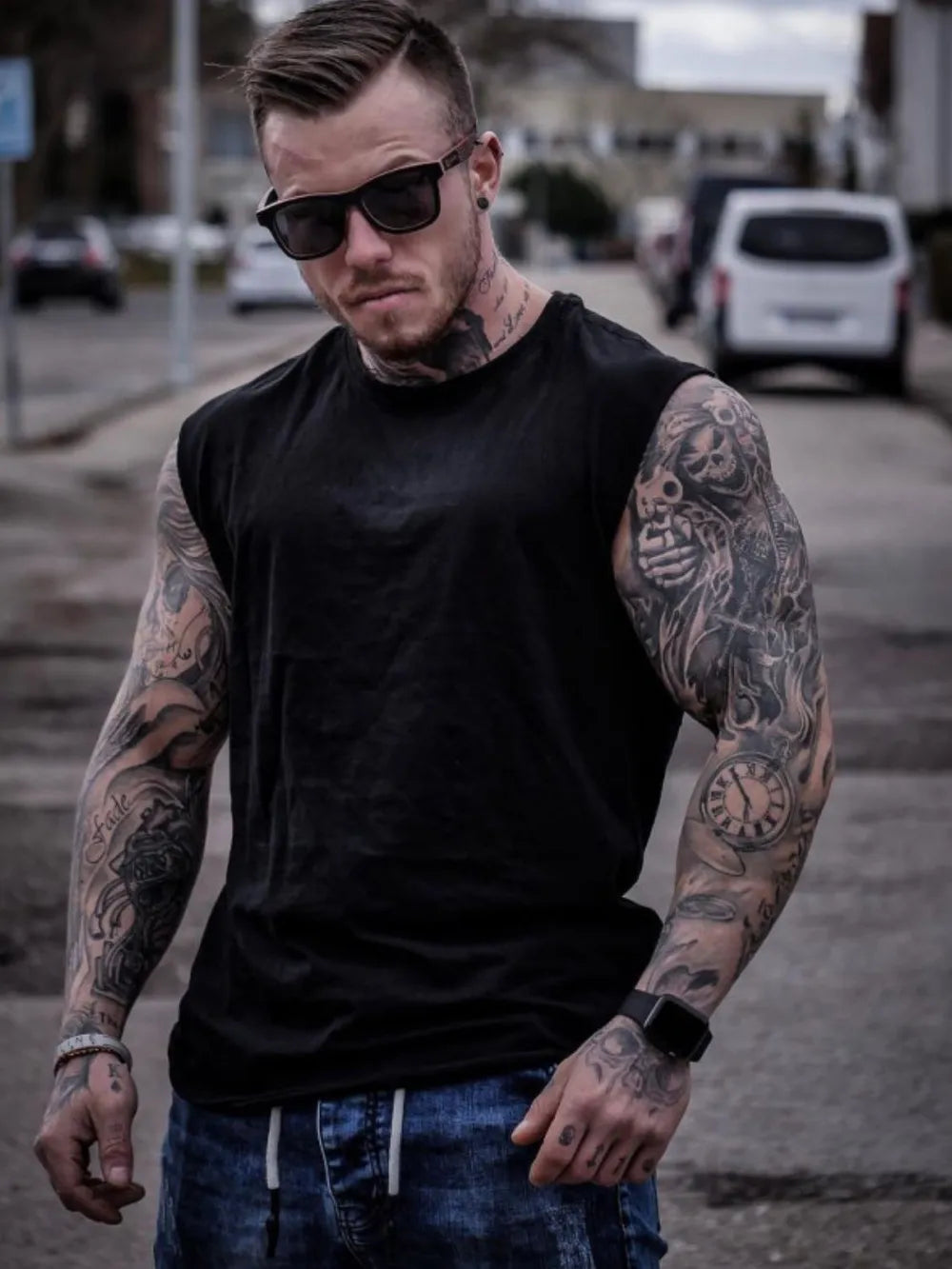 Black sleeveless muscle-fit tank top with a crew neck, worn by a tattooed man.