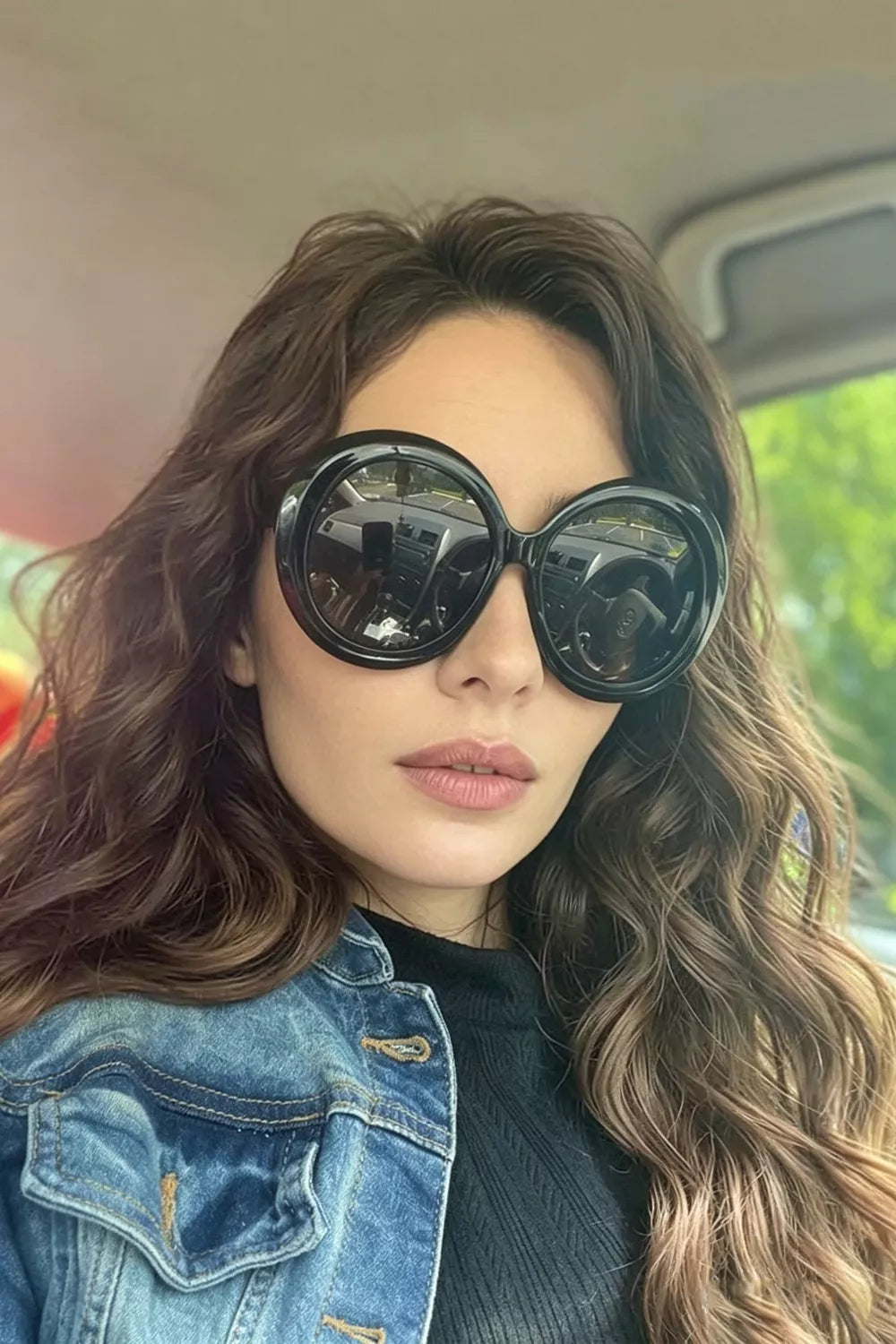 Chic oversized round black fashion sunglasses with bold frames, worn by a woman in a denim jacket.