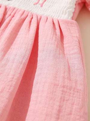 Embroidered teddy bear baby dress in pink cotton with smocked white bodice and gathered skirt.