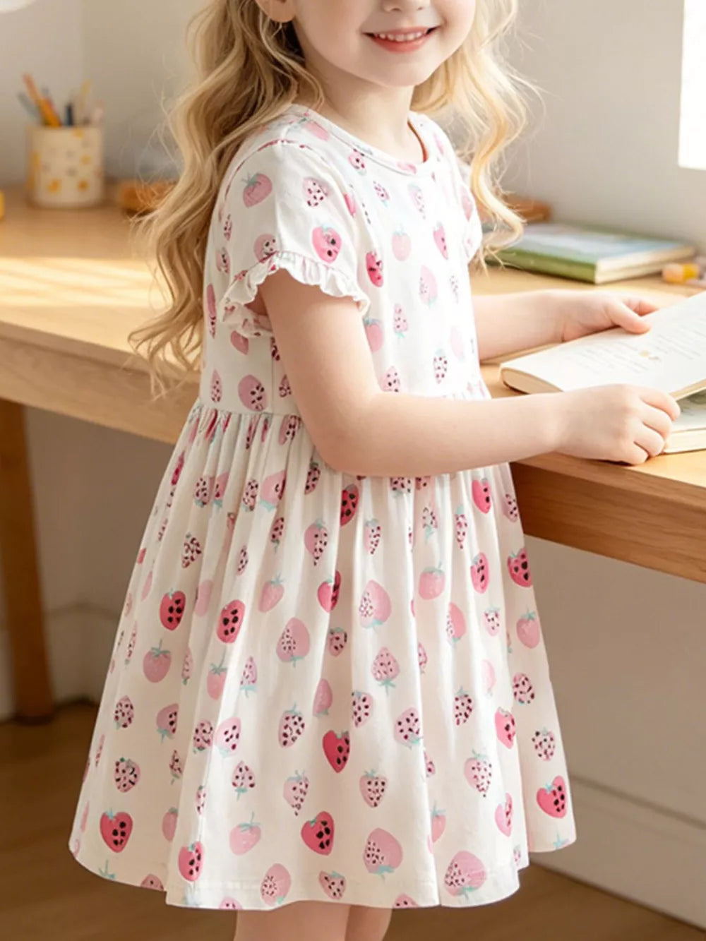 Toddler white cotton dress with strawberry print and ruffled sleeves.