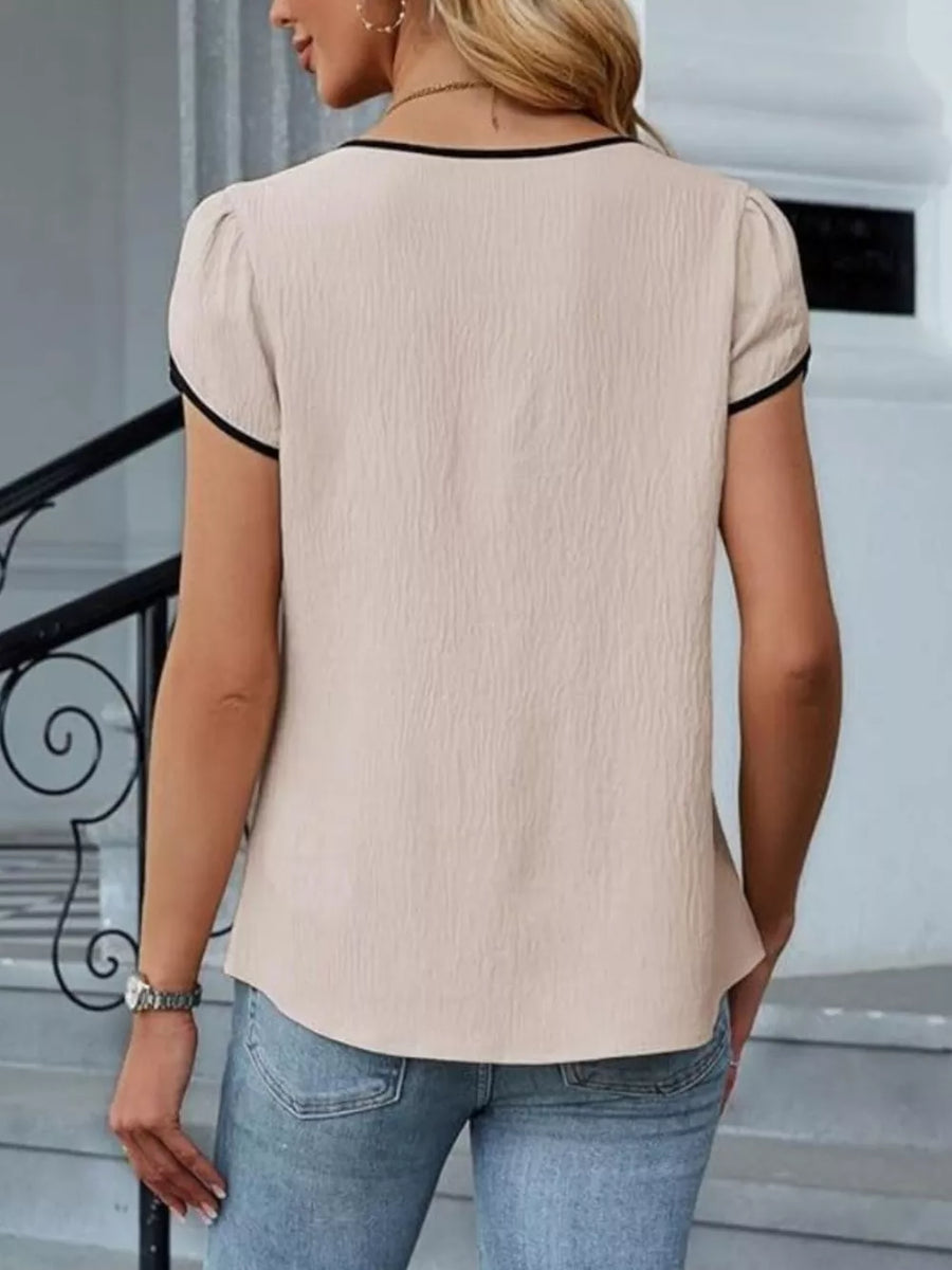 Apricot blouse with black trim, petal sleeves, and textured fabric.