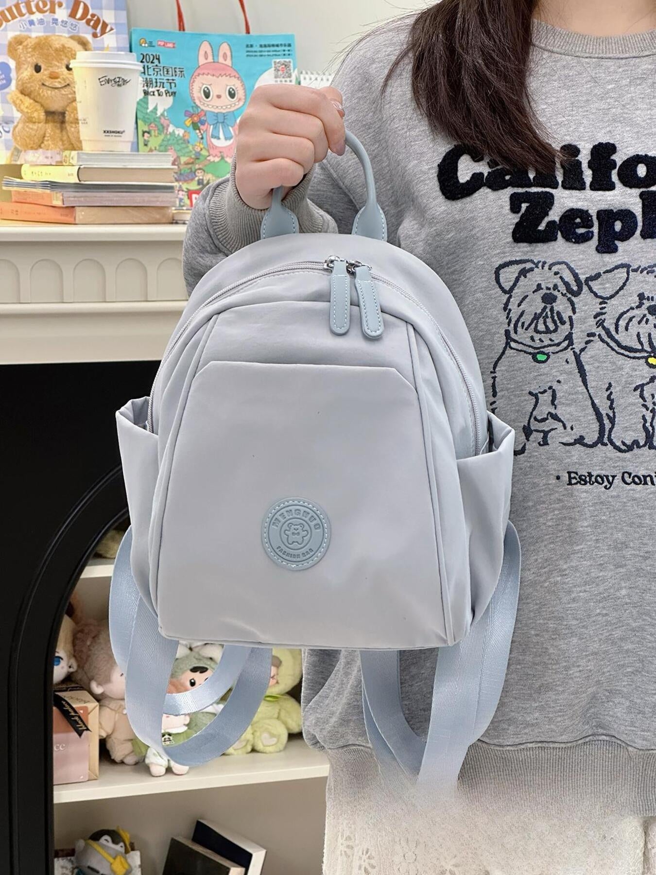 Mini nylon backpack in light blue with zippered pockets and a bear patch detail.