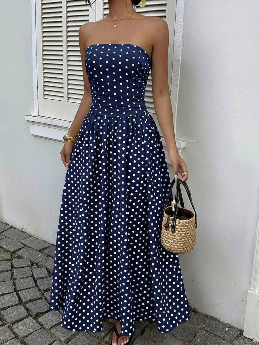 Navy polka dot A-line maxi dress with strapless neckline and cinched waist.