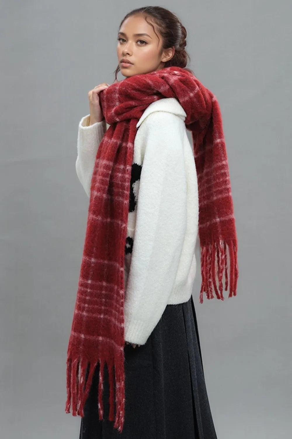 Textured plaid fringed scarf in deep red with white accents, styled with a cozy sweater.