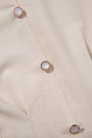 Elegant V-neck blouse in cream polyester with decorative pearl buttons and gold trim.