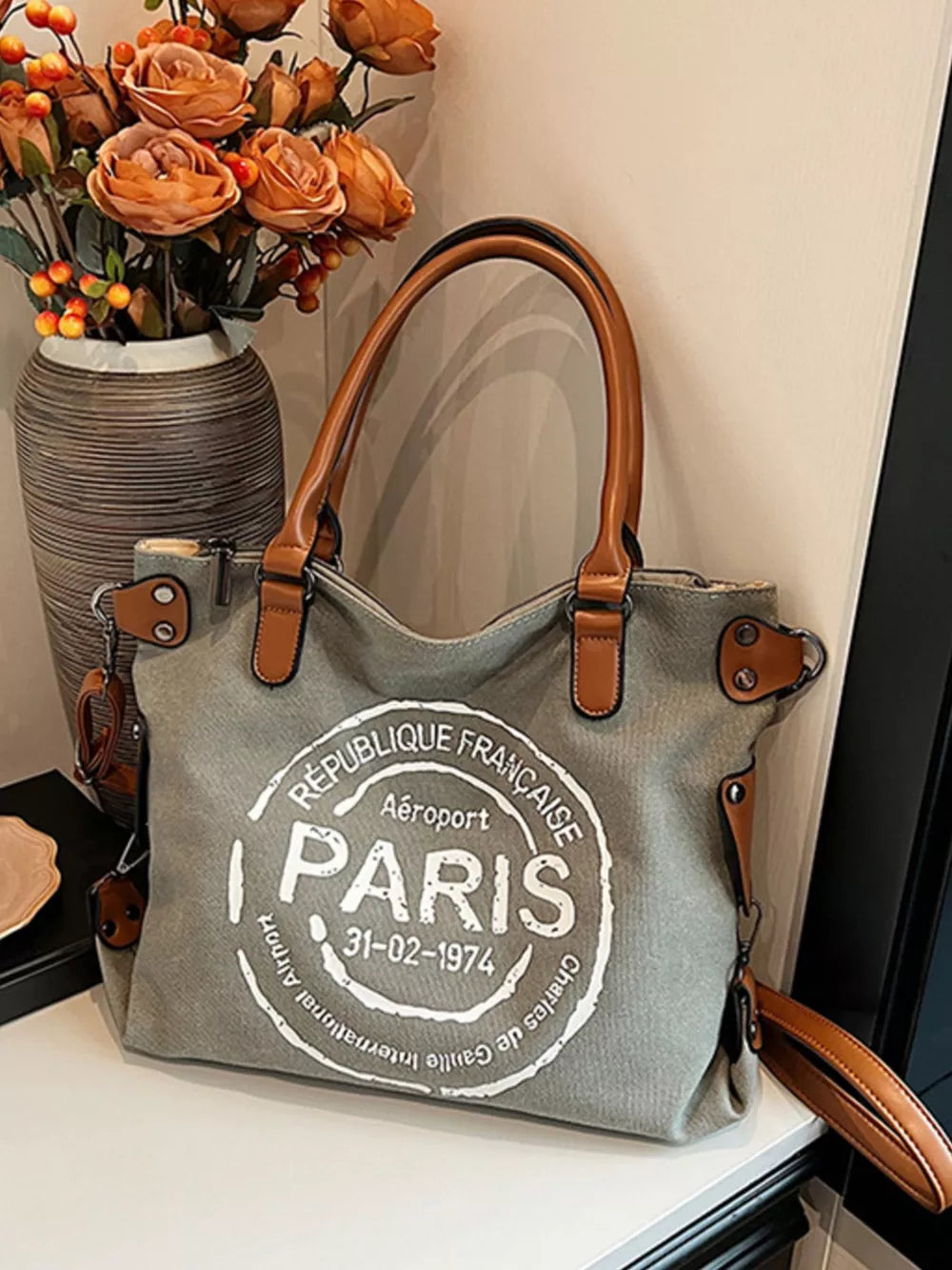 Parisian graphic tote bag in dark gray canvas with brown handles and airport stamp detail.