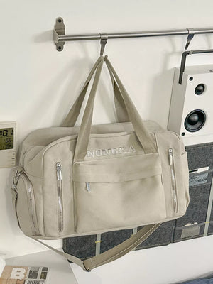 Beige canvas duffel bag with embroidered logo, zippered pockets, and adjustable crossbody strap.