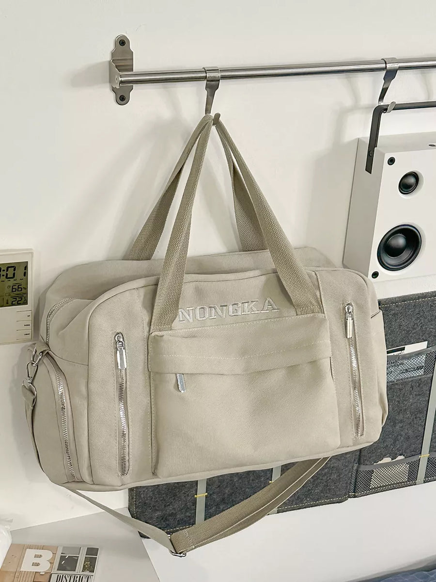 Beige canvas duffel bag with embroidered logo, zippered pockets, and adjustable crossbody strap.