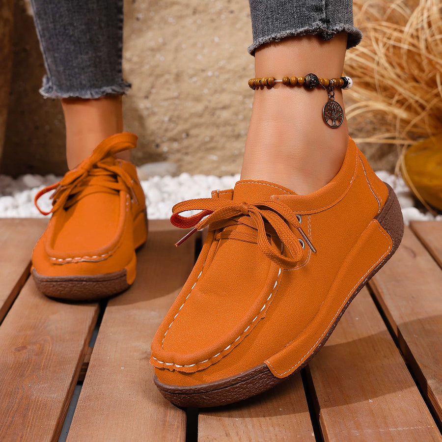 Orange lace-up moccasin style sneakers with white stitching and a brown sole.