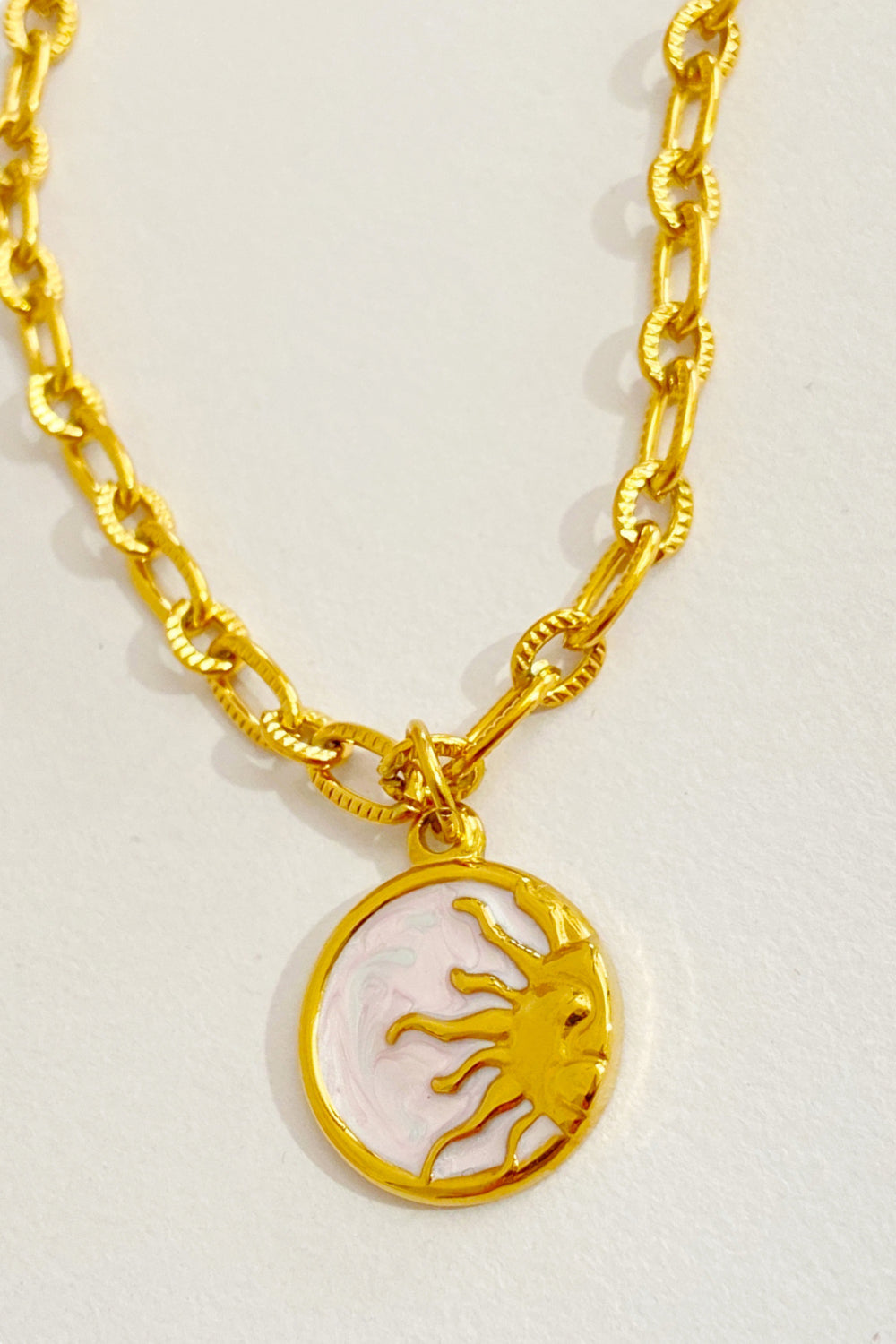Gold plated chain necklace with a sun charm on a marbled white background.