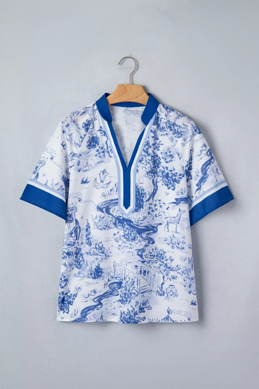 White polyester shirt with blue toile print, V-neck, short sleeves, and contrast trim.