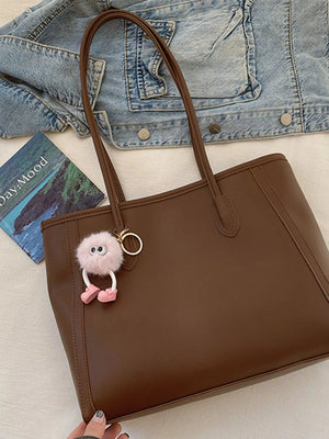 Brown PU leather tote bag with a fluffy pink charm and a denim jacket.