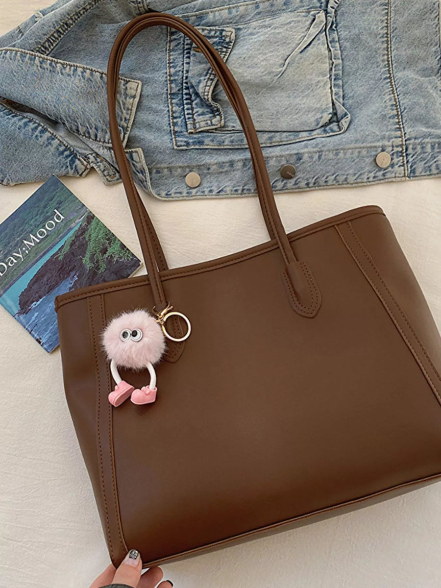 Brown PU leather tote bag with a fluffy pink charm and a denim jacket.