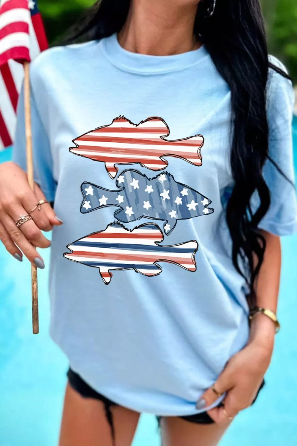 Light blue t-shirt with patriotic fish graphic featuring red, white, and blue stripes and stars.