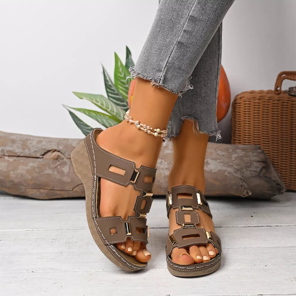Brown open-toe wedge sandals with decorative gold buckles and cut-out details.