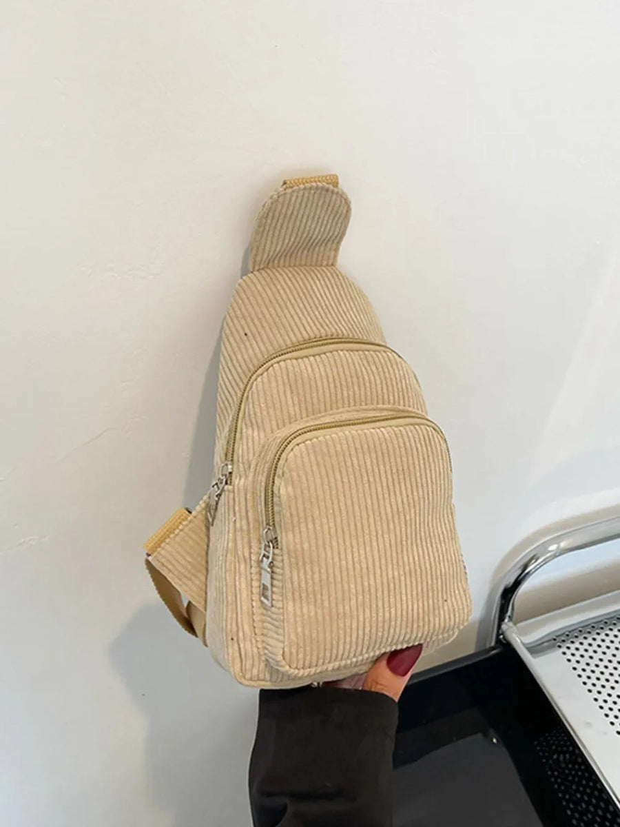 Khaki corduroy sling bag with zip pockets and adjustable strap.