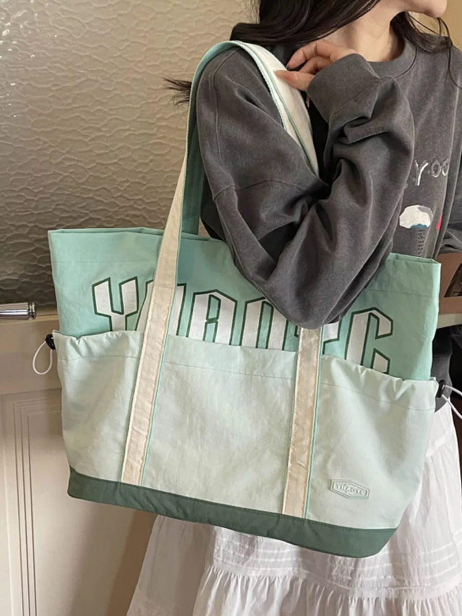 Green drawstring shoulder bag with bold white lettering and side pockets.