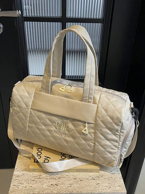 Diamond-stitched beige quilted duffel bag with adjustable strap and front logo detail.
