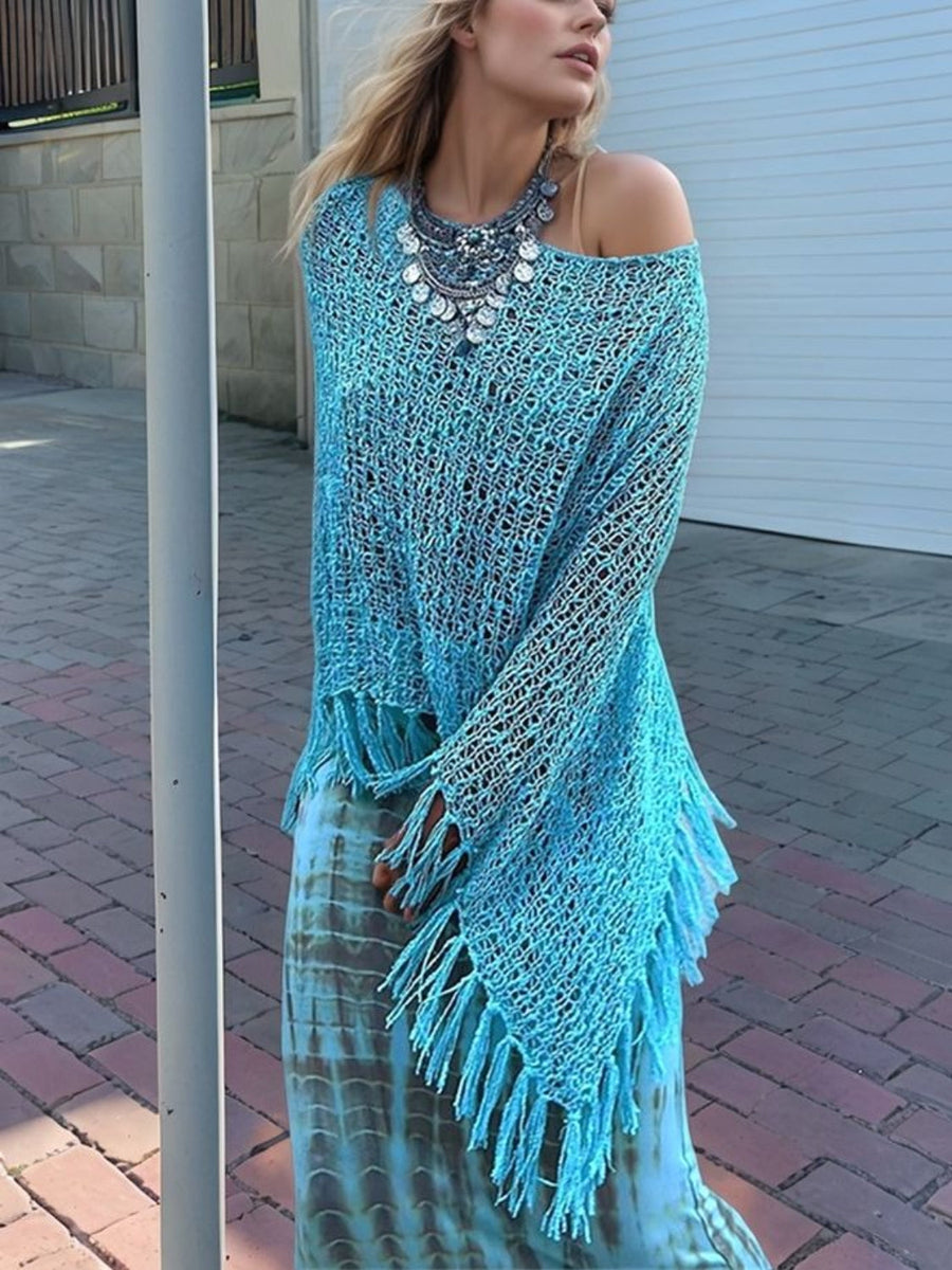 Sky blue open-knit acrylic boat neck poncho with fringe trim, styled with a statement necklace.