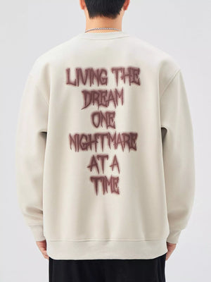 Oversized crew-neck sweatshirt in light beige with dark red "Living the dream one nightmare at a time" graphic on back.