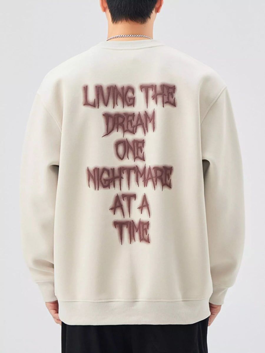 Oversized crew-neck sweatshirt in light beige with dark red "Living the dream one nightmare at a time" graphic on back.