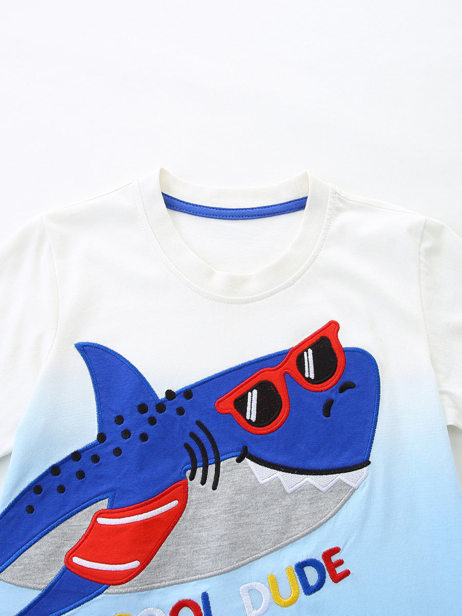 White cotton toddler tee with blue ombre and a shark wearing sunglasses graphic.