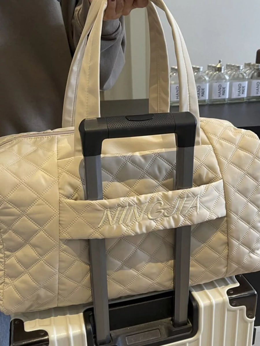 Diamond-stitched beige quilted duffel bag with embroidered name detail.