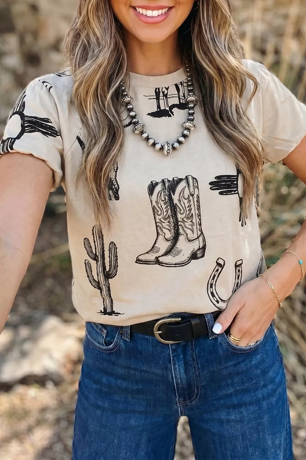 T-shirt with western graphics including boots, cactus, and horseshoe on a light tan crew neck tee.