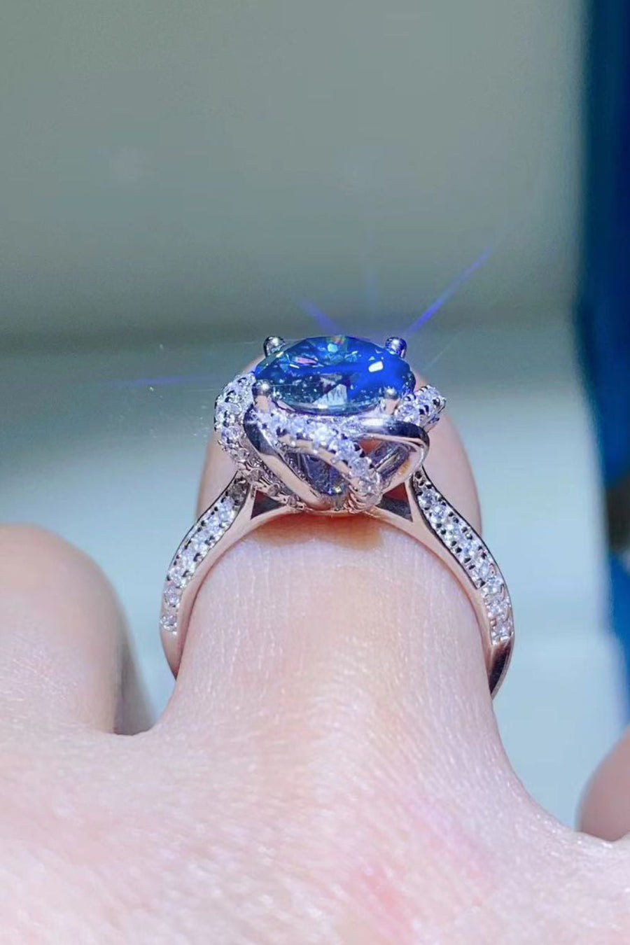 Blue moissanite halo ring with diamond band on finger
