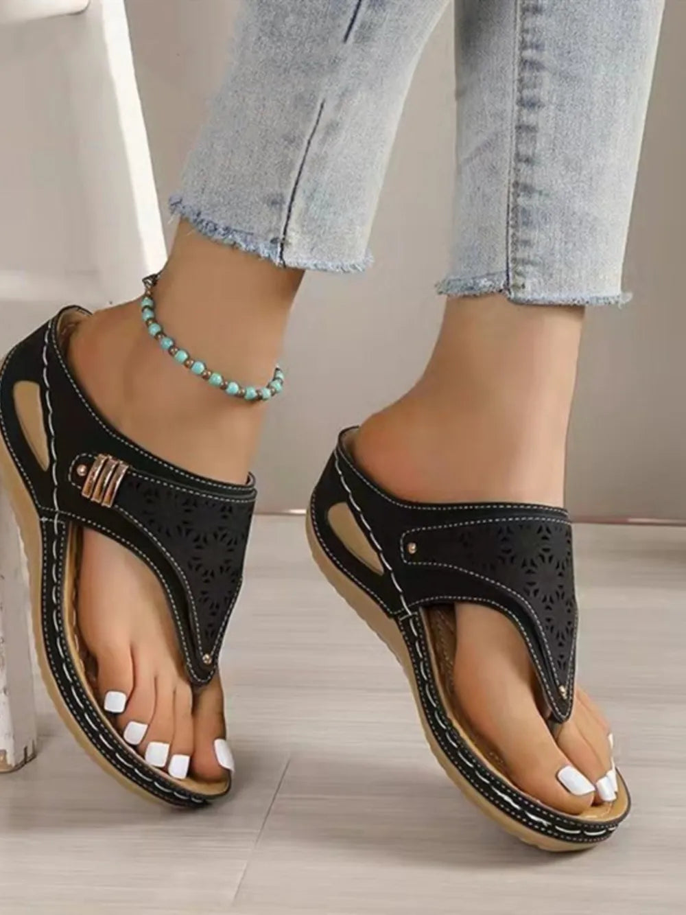Black laser-cut thong sandals with decorative stitching and a gold buckle detail.