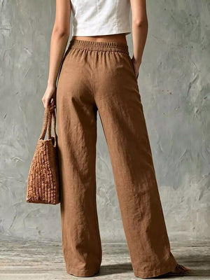 Brown linen wide-leg pants with elastic waist and pockets, styled with a woven bag.