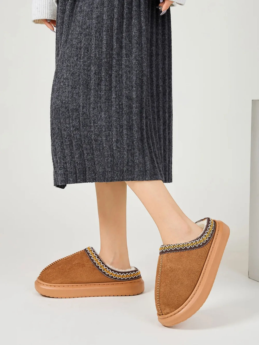Caramel shearling house slippers with embroidered trim and faux fur lining.