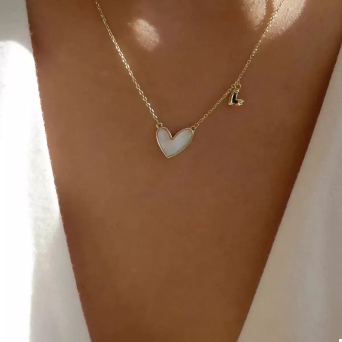 Gold dainty necklace with white alloy heart pendant and small black letter L charm.