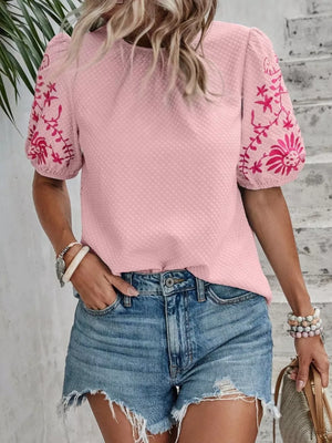 Pink embroidered puff sleeve blouse with textured fabric and floral sleeve detail.