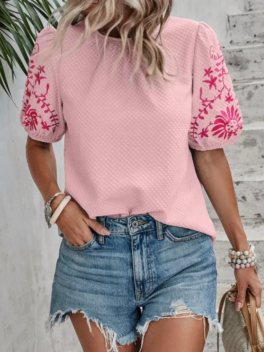 Pink embroidered puff sleeve blouse with textured fabric and floral sleeve detail.